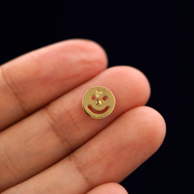 A yellow gold Smiley Face Earring laying facedown on a model's fingers to show the underside view