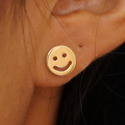 Close up view of a model's ear wearing a yellow gold Smiley Face Earring