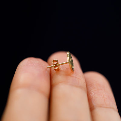 A 14k gold Smiley Face Earring sitting sideways on a model's fingertips to show detail