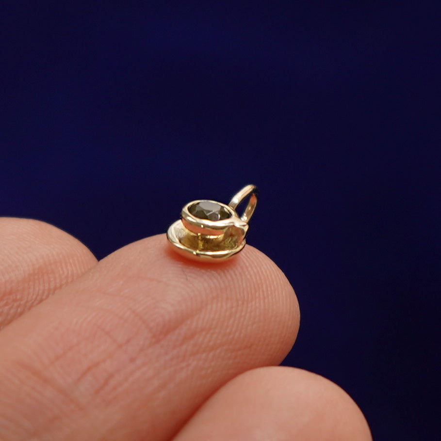 Alternate side view of a 14k gold coffee cup charm on a model's fingertip