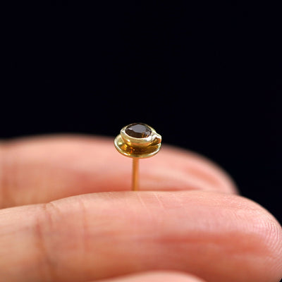 A solid gold Coffee Cup Earring standing upright between a model's fingers to show the side detail
