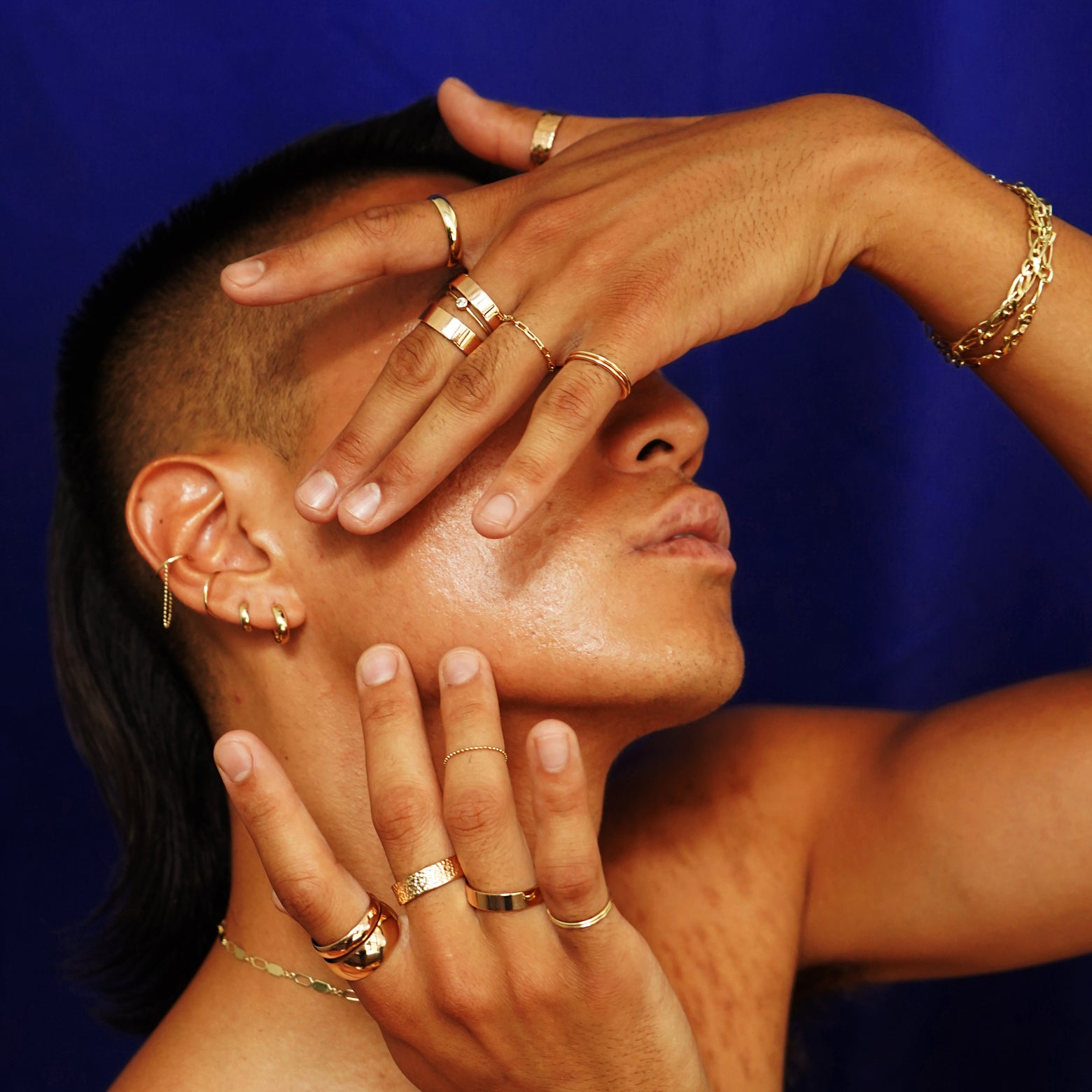A model with head tilted up and their hands raised over their face wearing various Automic Gold jewelry