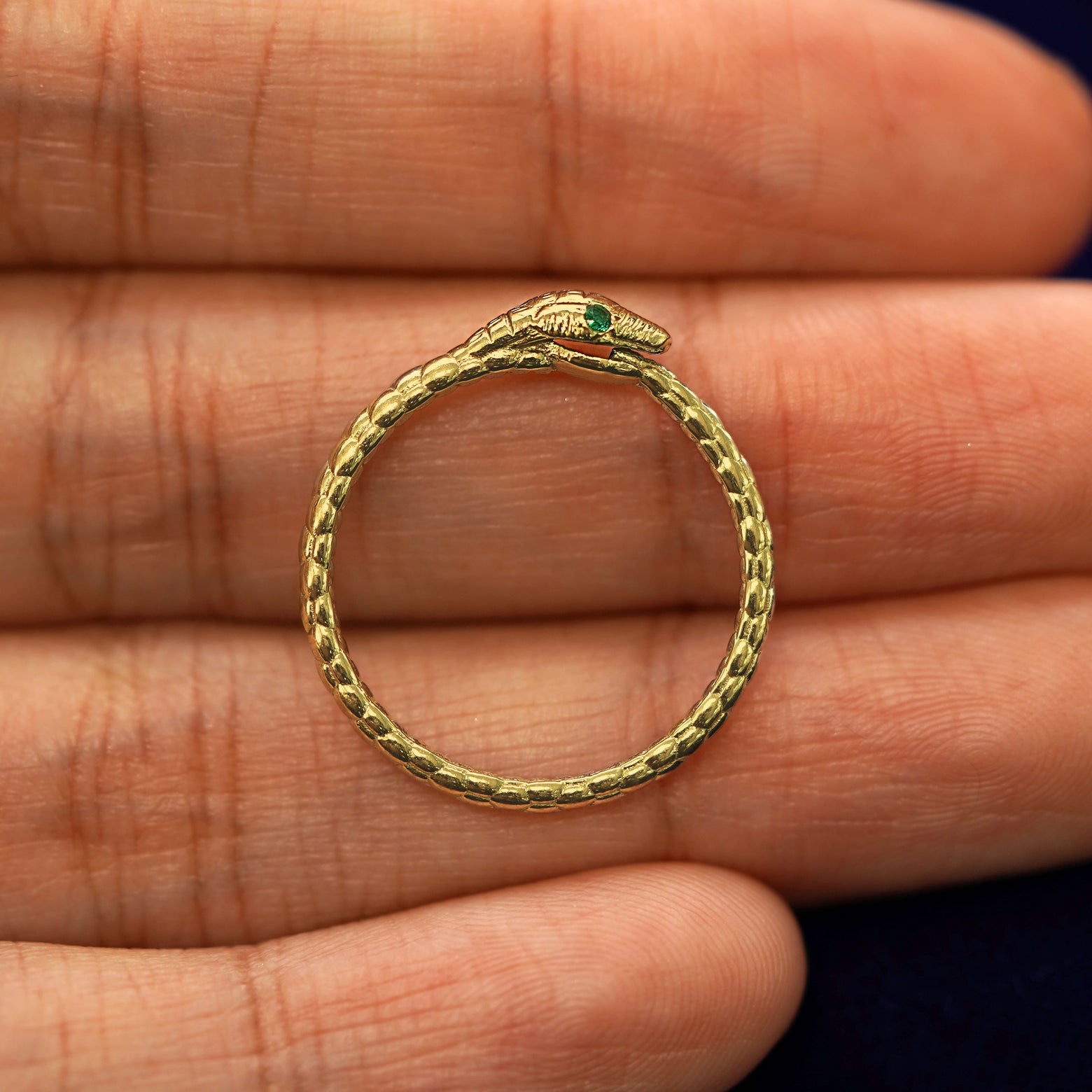 A yellow gold emerald Gemstone Ouroboros Snake RIng in a model's hand showing the thickness of the band
