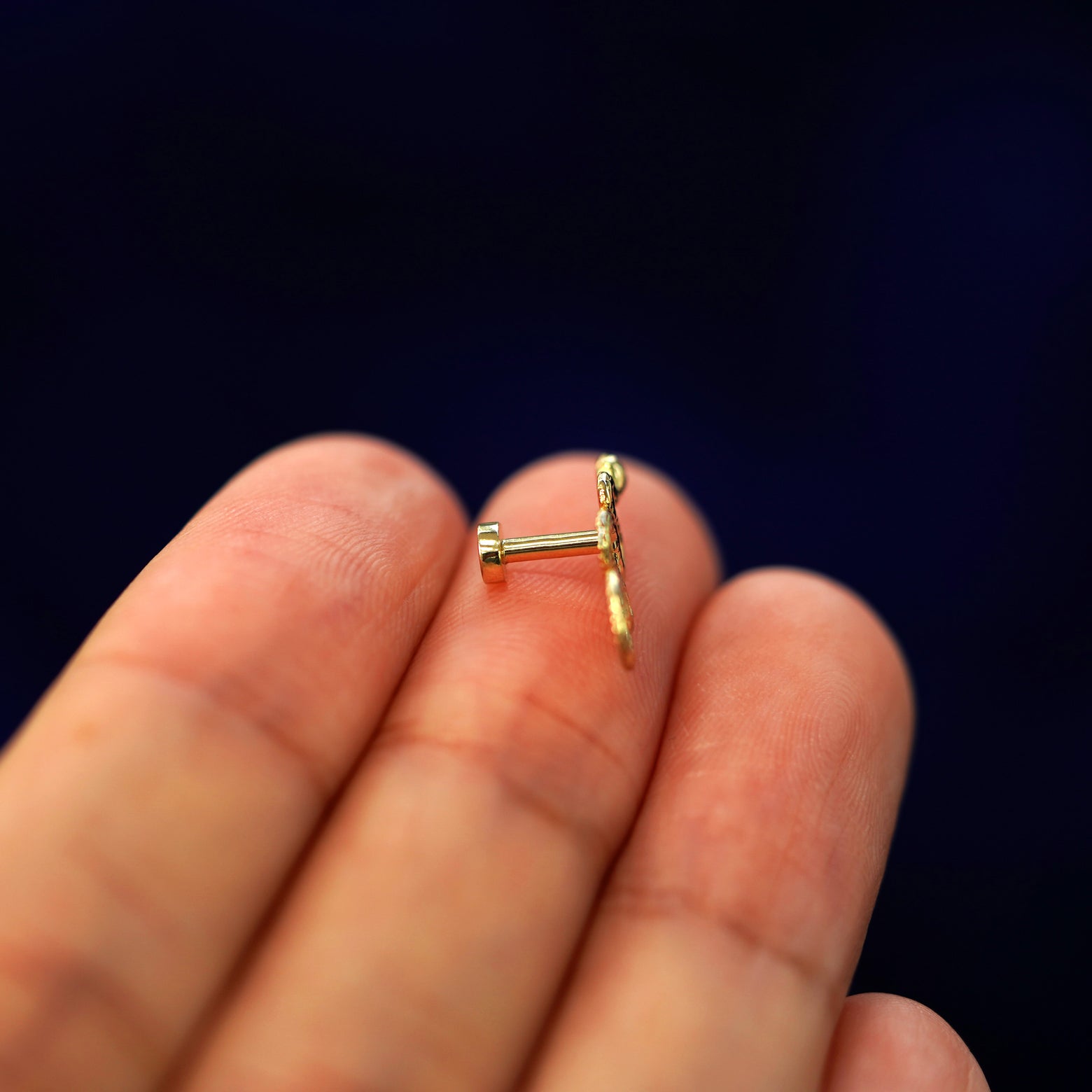 Side view of a yellow gold Snake Flatback Piercing on a model's fingertips