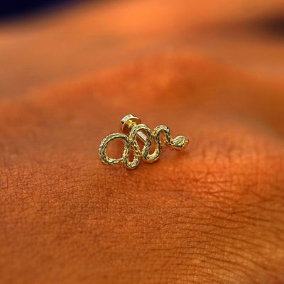 A solid 14k yellow gold Snake Flatback Piercing resting on the back of a model's hand