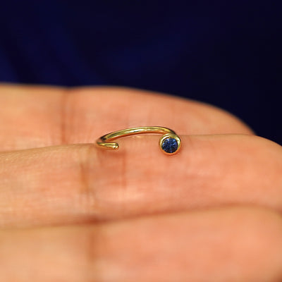 A 14k yellow gold sapphire Gemstone Open Hoop resting on a models fingertip to show the open part of the earring