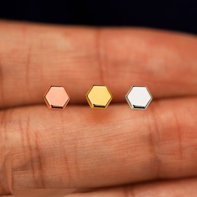 Three versions of the Hexagon Earring in options of yellow, white, and rose gold in between a model's fingers