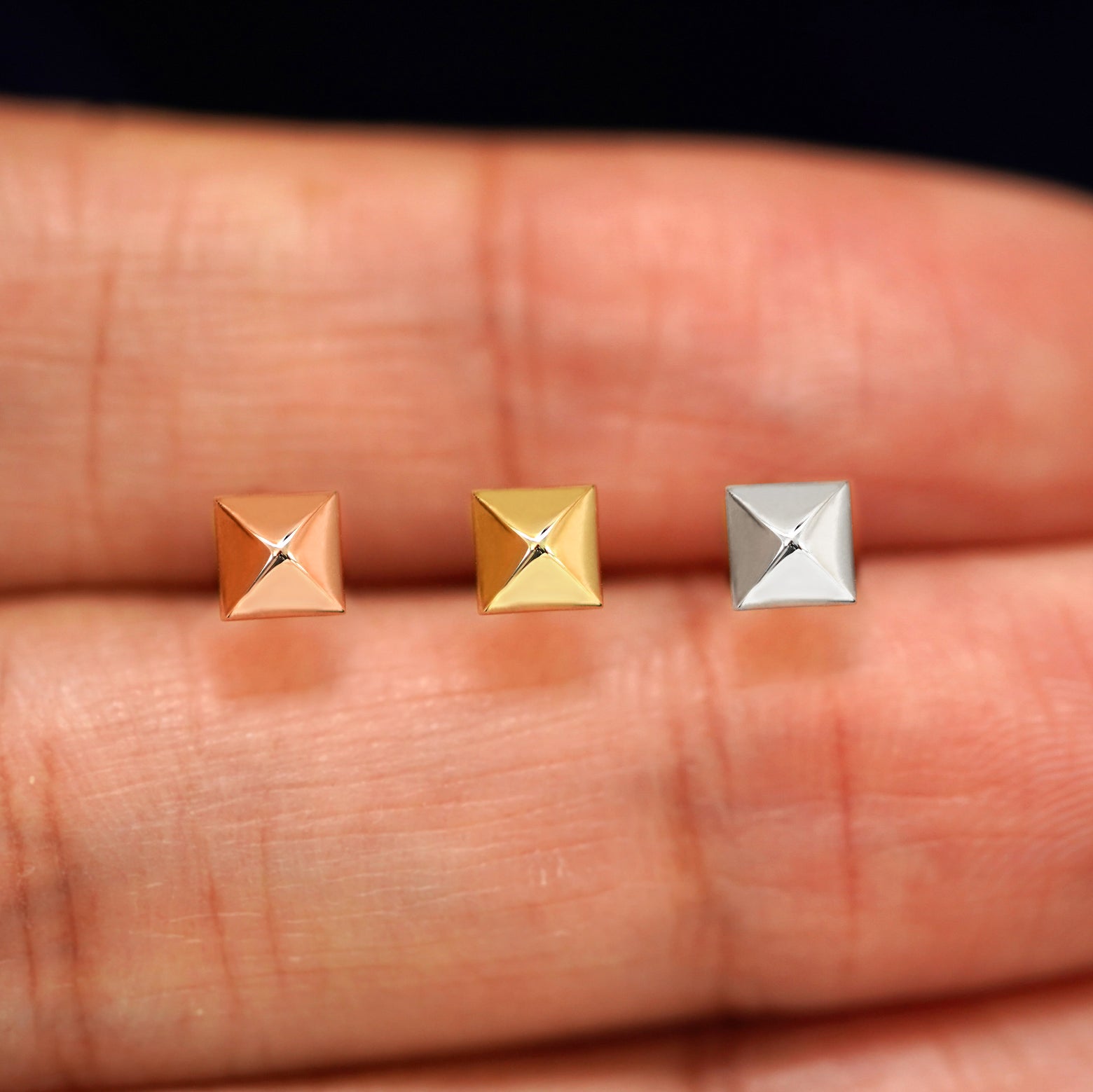 Three versions of the Pyramid Earring in options of yellow, white, and rose gold in between a model's fingers