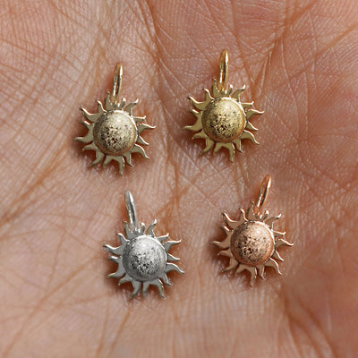 Four versions of the Sun Charm in yellow, white, rose, and champagne gold resting in a model's palm