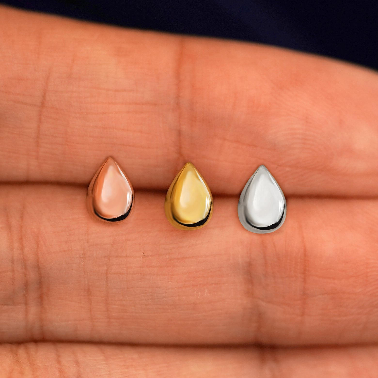 Three versions of the Teardrop Earring in options of yellow, white, and rose gold in between a model's fingers