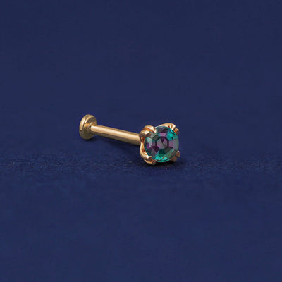A 14 karat solid gold Alexandrite Flat Back Earring on a dark blue background