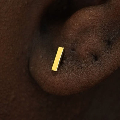 Close up view of a model's ear wearing a 14k yellow gold Bar Stud Earring