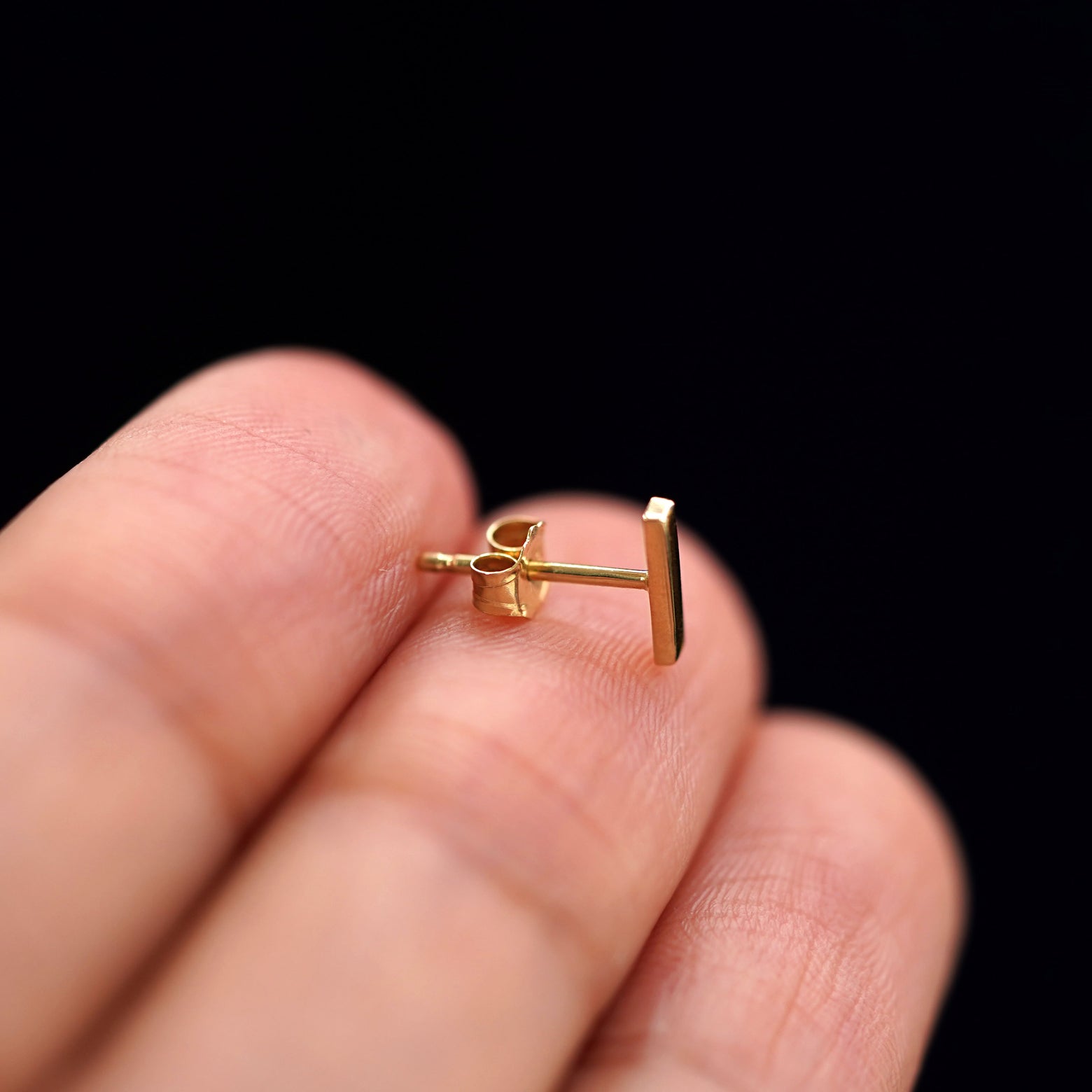 Side view of a 14k gold Bar Earring with a standard pushback backing on a model's finger