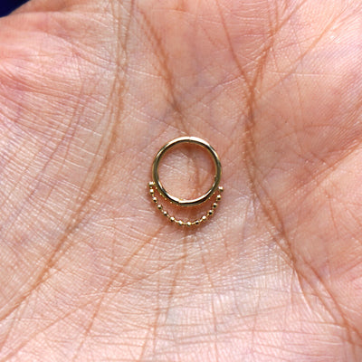 A model holding a closed yellow gold Beaded Huggie Hoop in their palm