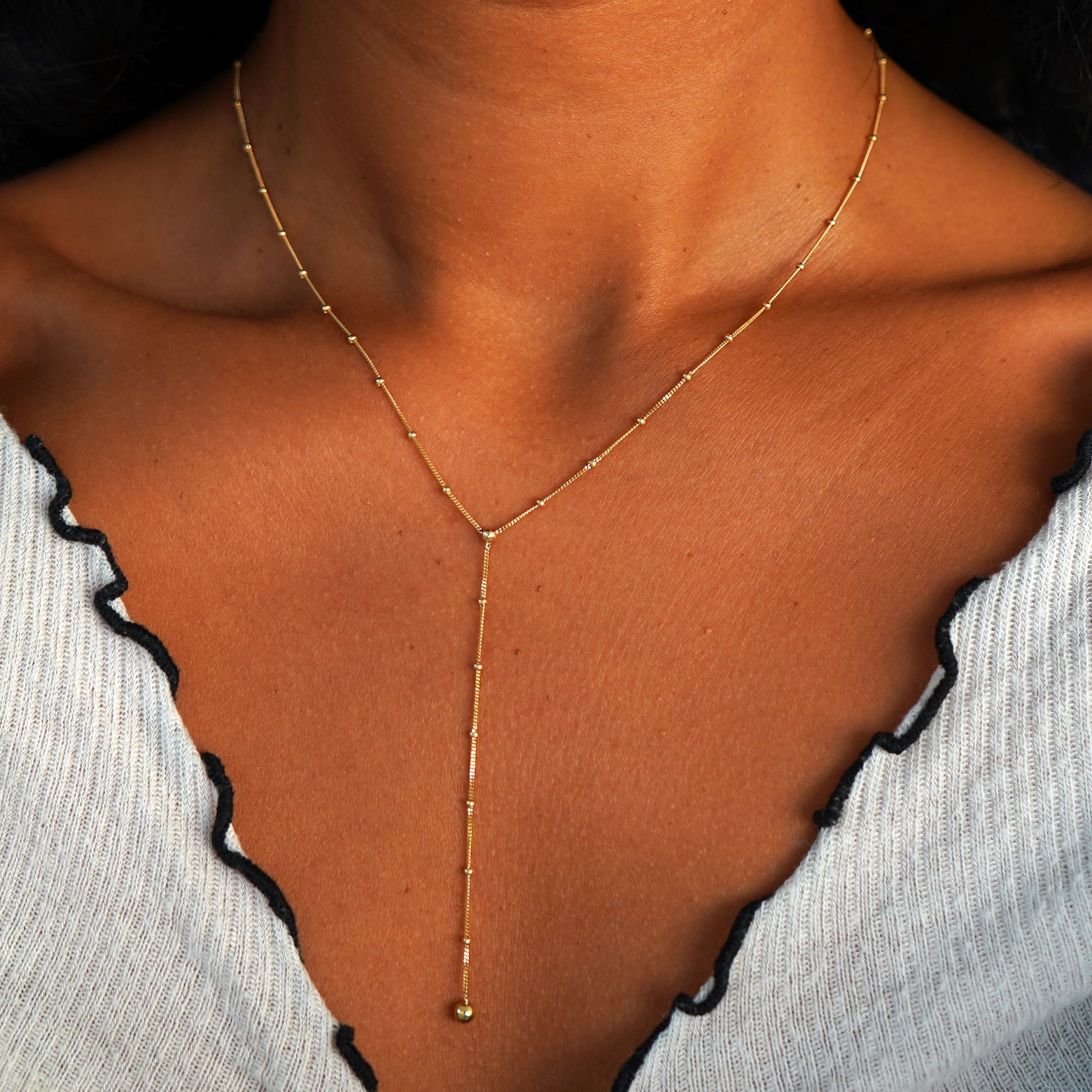 Close up view of a model's neck wearing a yellow gold Beaded Essential Lariat Necklace