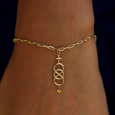 A model's wrist wearing a yellow gold Bisexual Symbol Charm on a Butch Bracelet