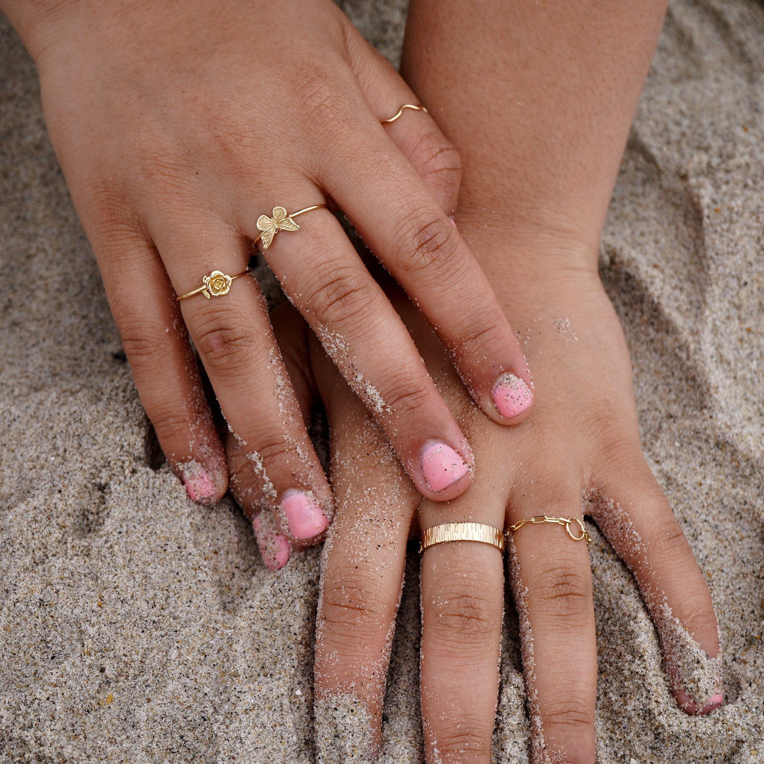 A model with their hands in the sand at the beach wearing various Automic Gold rings including a Butterfly Ring