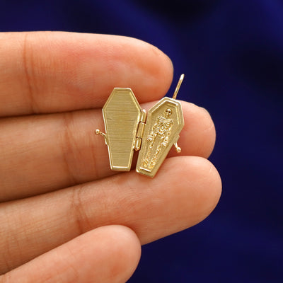 An open 14k gold Coffin Charm for chain held on a model's fingers