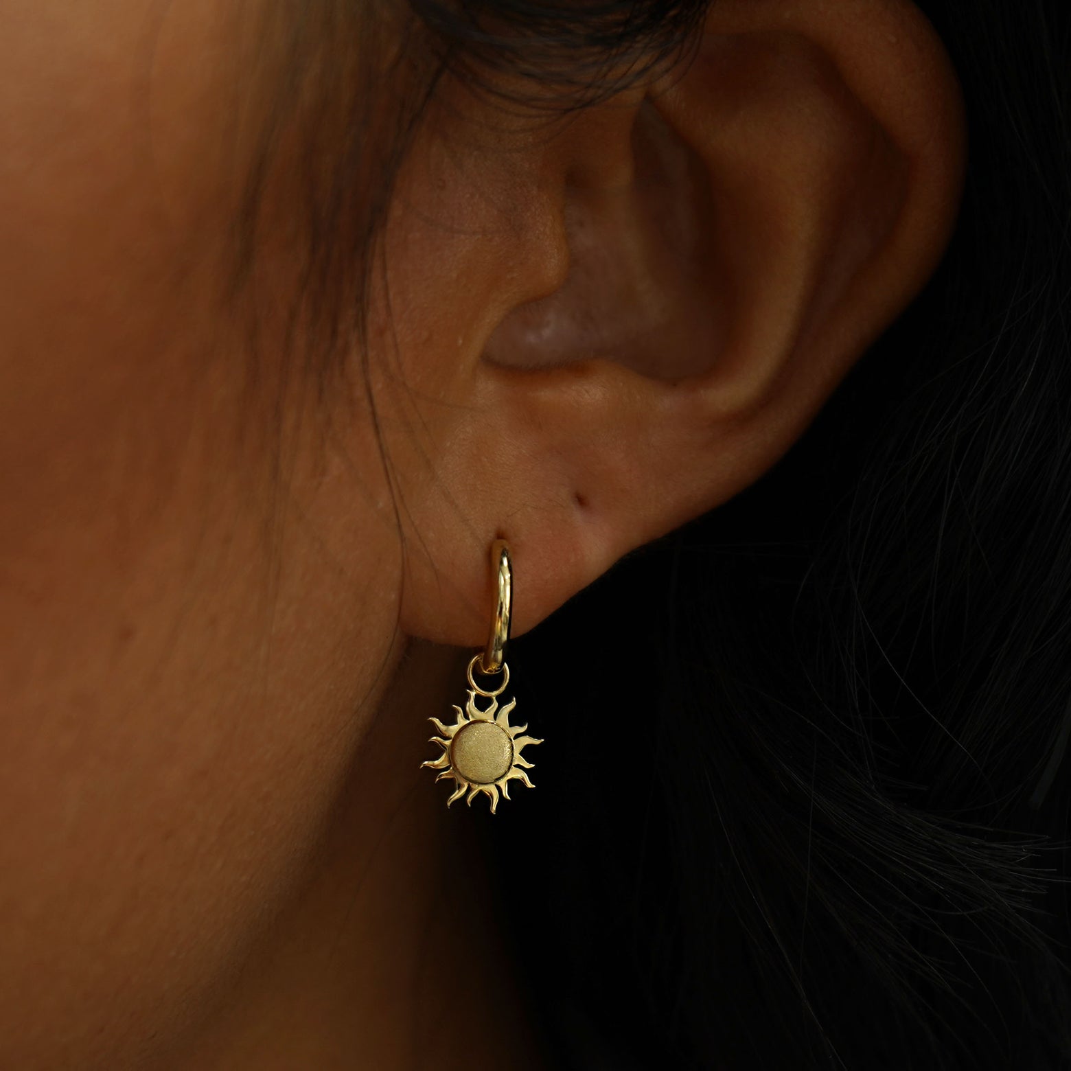 A model's ear wearing a 14k solid gold Sun Charm on a Curvy Huggie Hoop