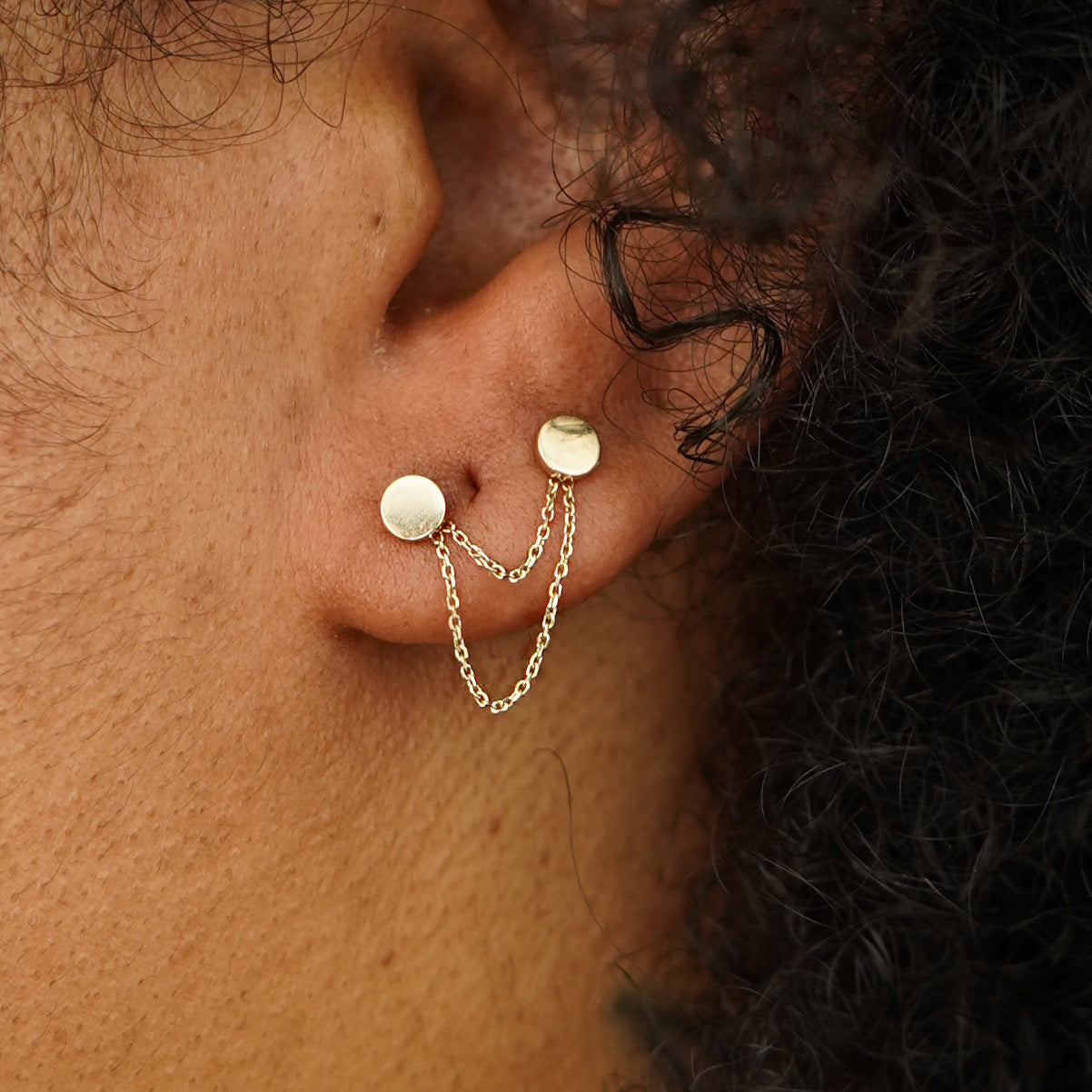 A model's ear wearing two Circle Studs with a yellow gold Cable Chain Connector in front of their lobe