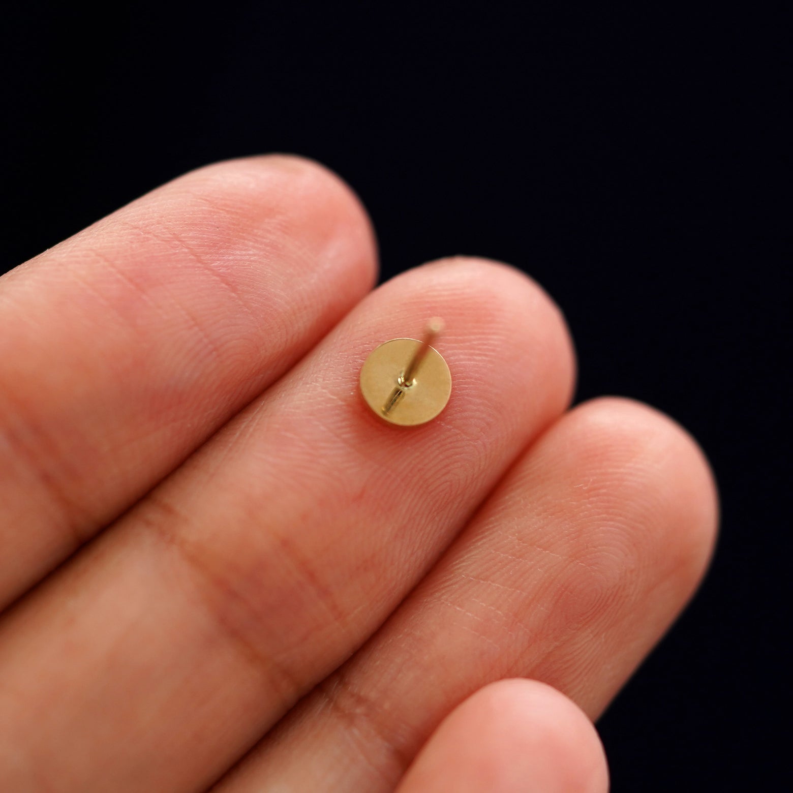 A yellow gold Medium Circle Earring laying facedown on a model's fingers to show the underside view