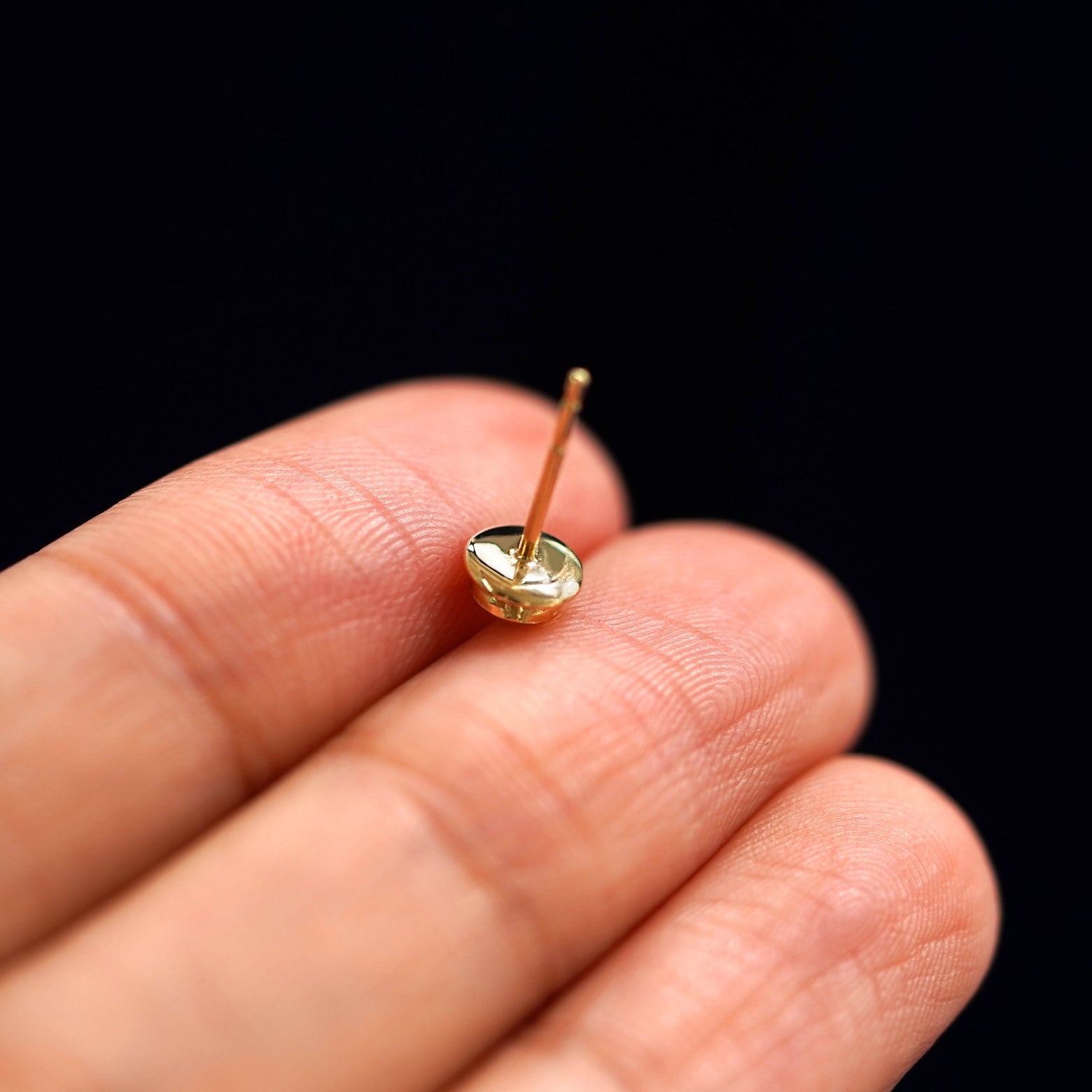 A yellow gold Coffee Cup Earring laying facedown on a model's fingers to show the underside view