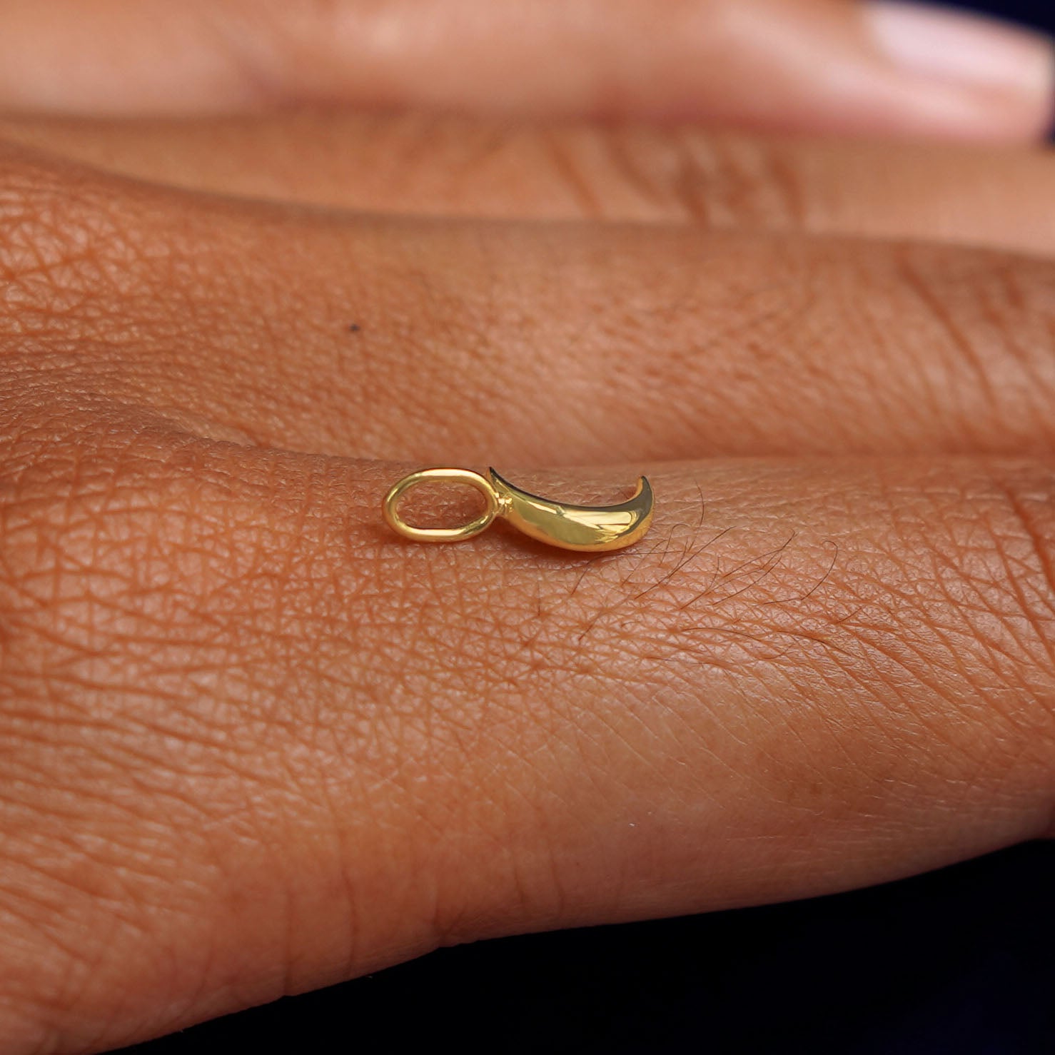 A 14k yellow gold Moon Charm for chain balancing on the back of a model's finger