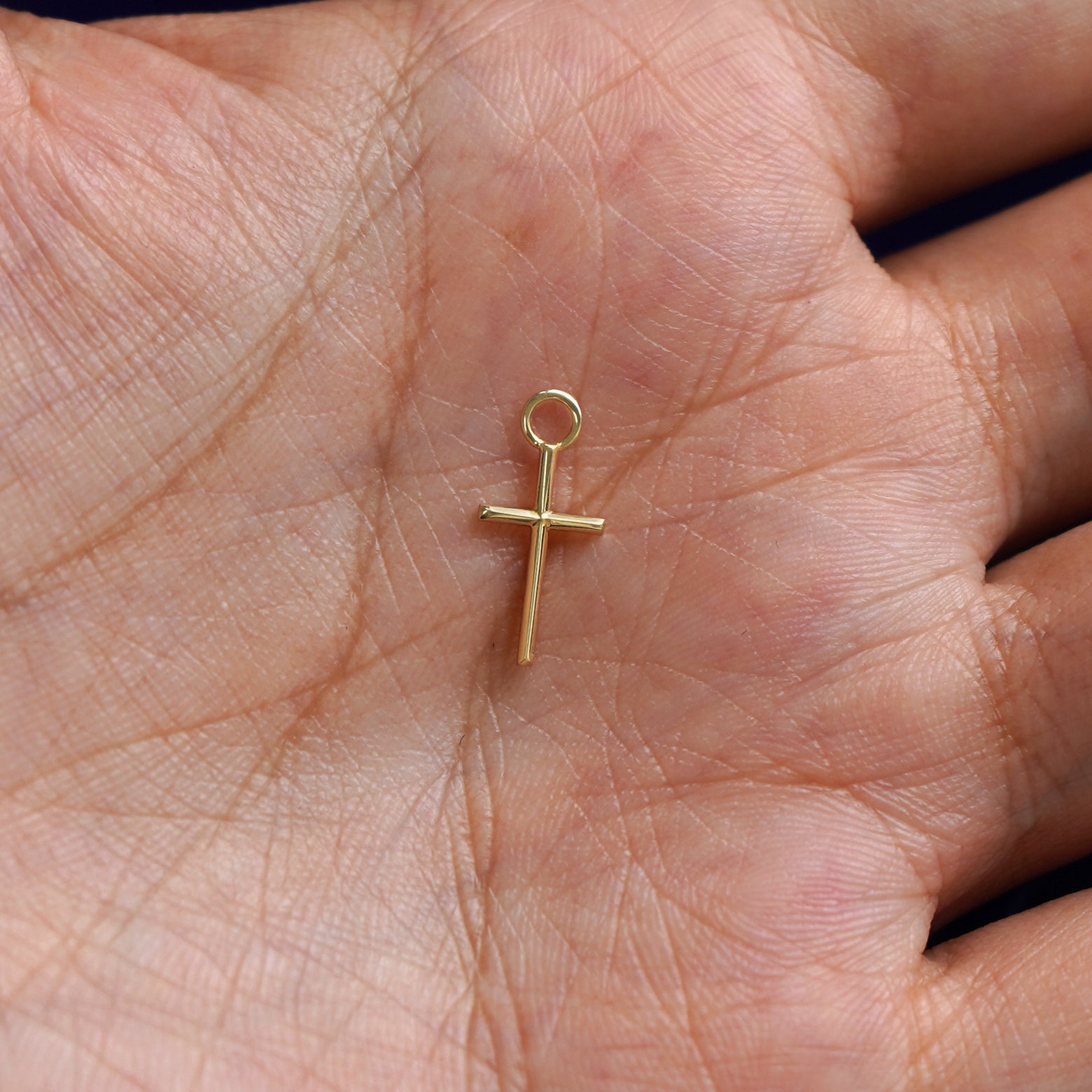 A solid gold Cross Charm for earring resting in a model's palm