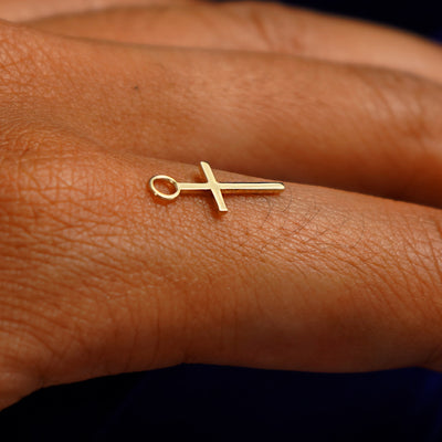 A 14k yellow gold Cross Charm for earring balancing on the back of a model's finger