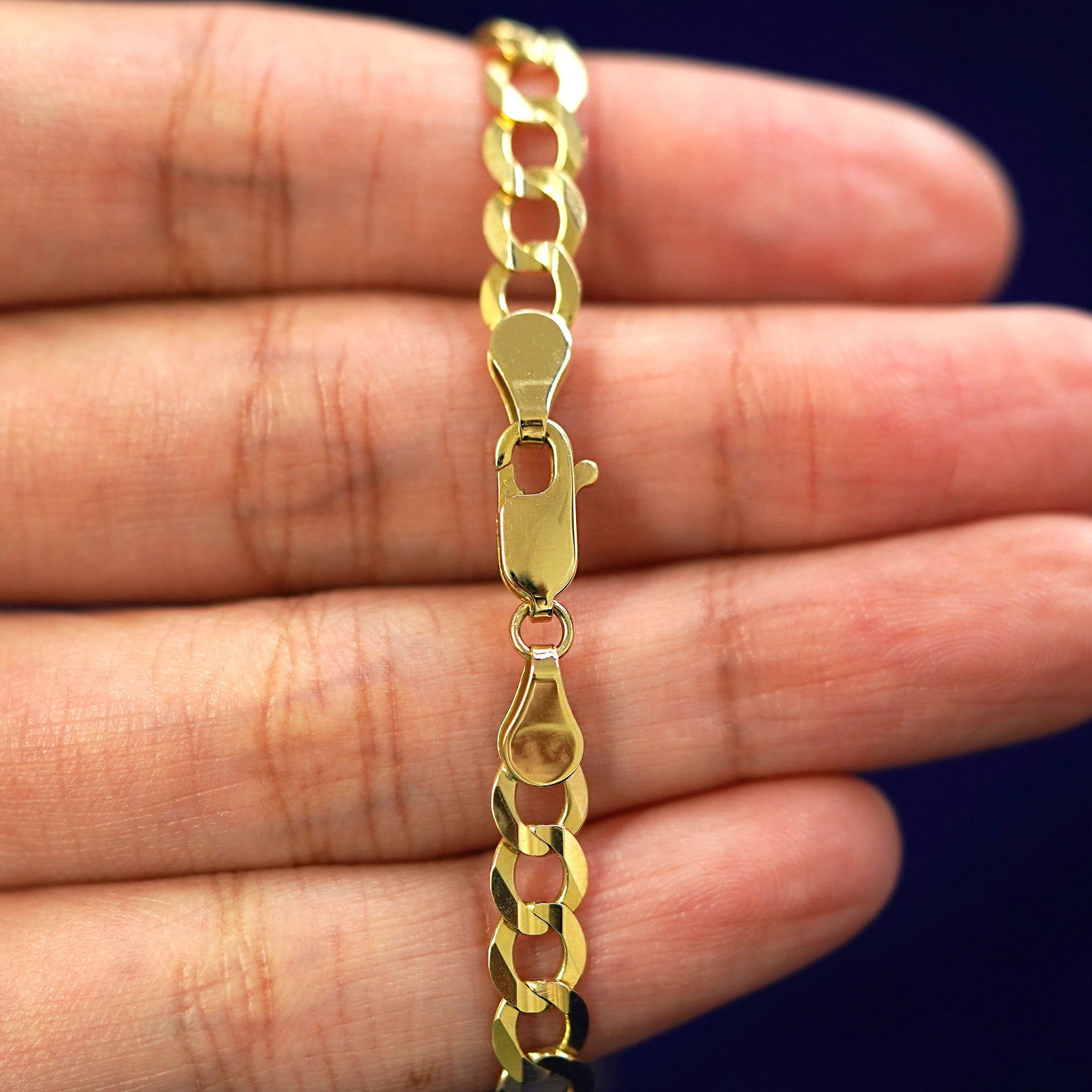 A model holding a 14k yellow gold Curb Anklet to show the lobster claw clasp