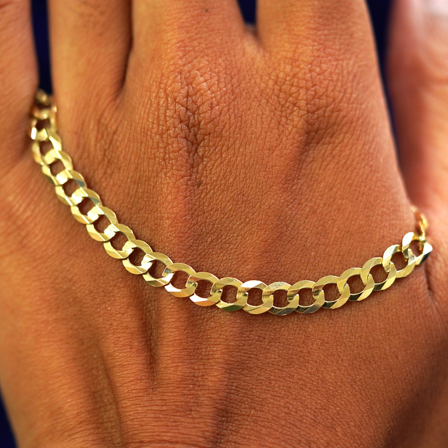 A solid gold Curb Chain resting on the back of a model's hand