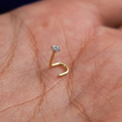 A 14 karat yellow gold Diamond Nose Stud standing upright to show detail and resting in the palm of a model's hand