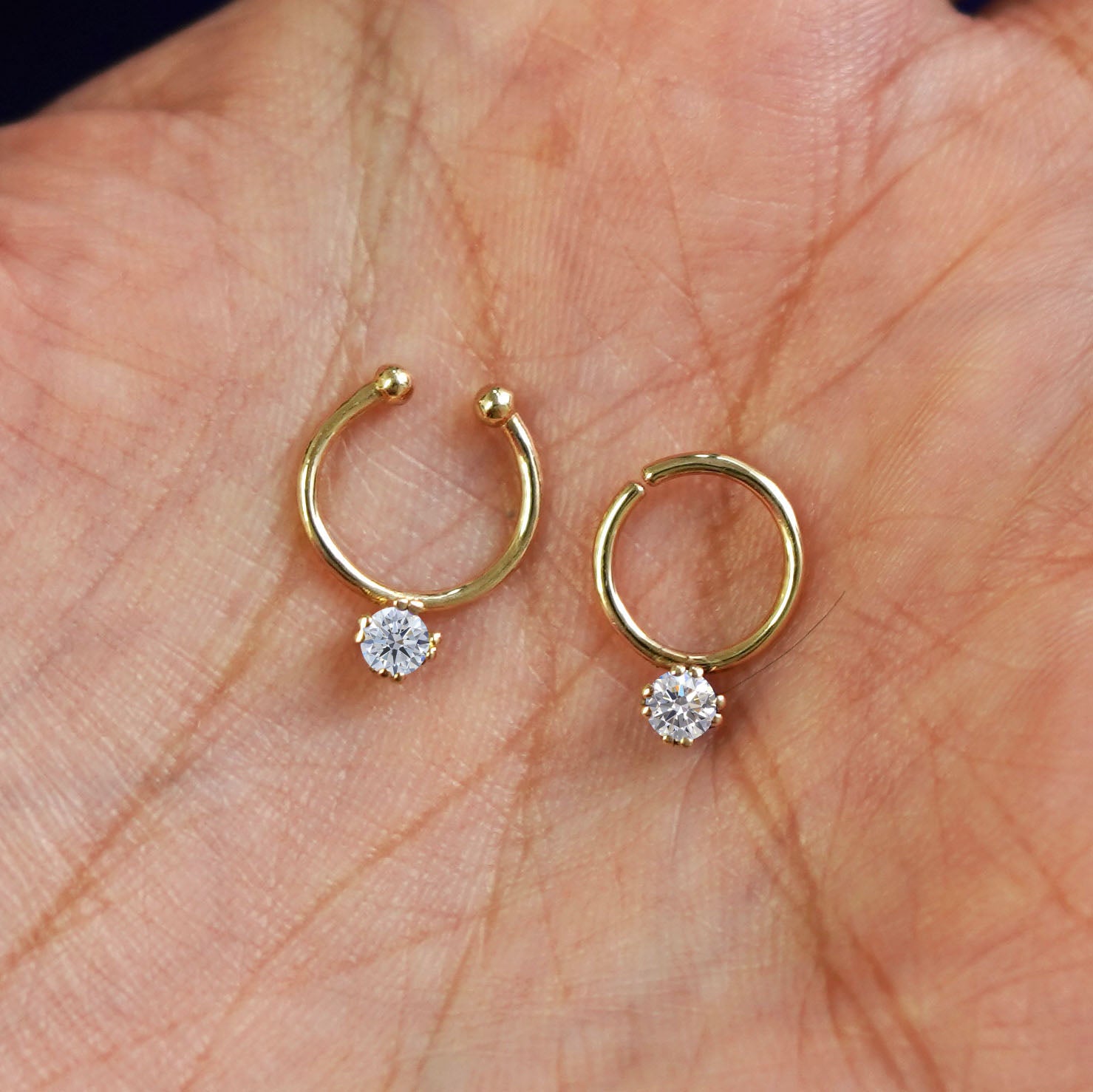 One Non-Pierced diamond and one Pierced diamond Septum ring both in 8mm resting in the palm of a model's hand