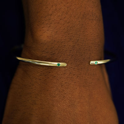 A model's wrist wearing a yellow gold emerald Open Bangle