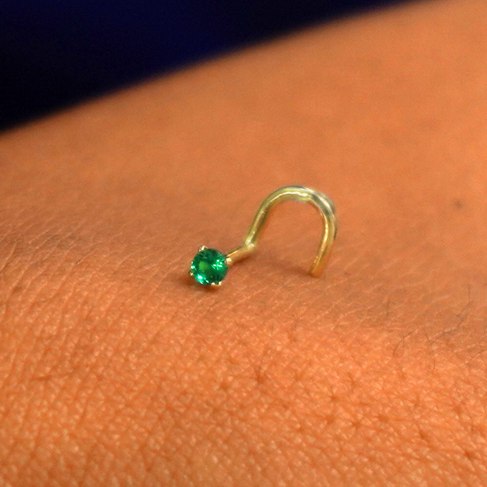 Close up view of a single 14k solid gold emerald Gemstone Nose Stud resting on the back on a model's hand