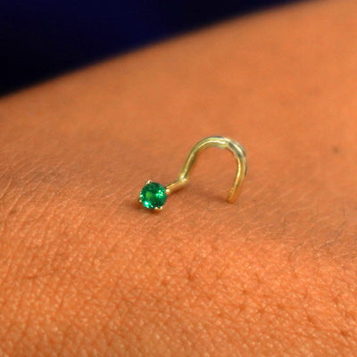 Close up view of a single 14k solid gold emerald Gemstone Nose Stud resting on the back on a model's hand