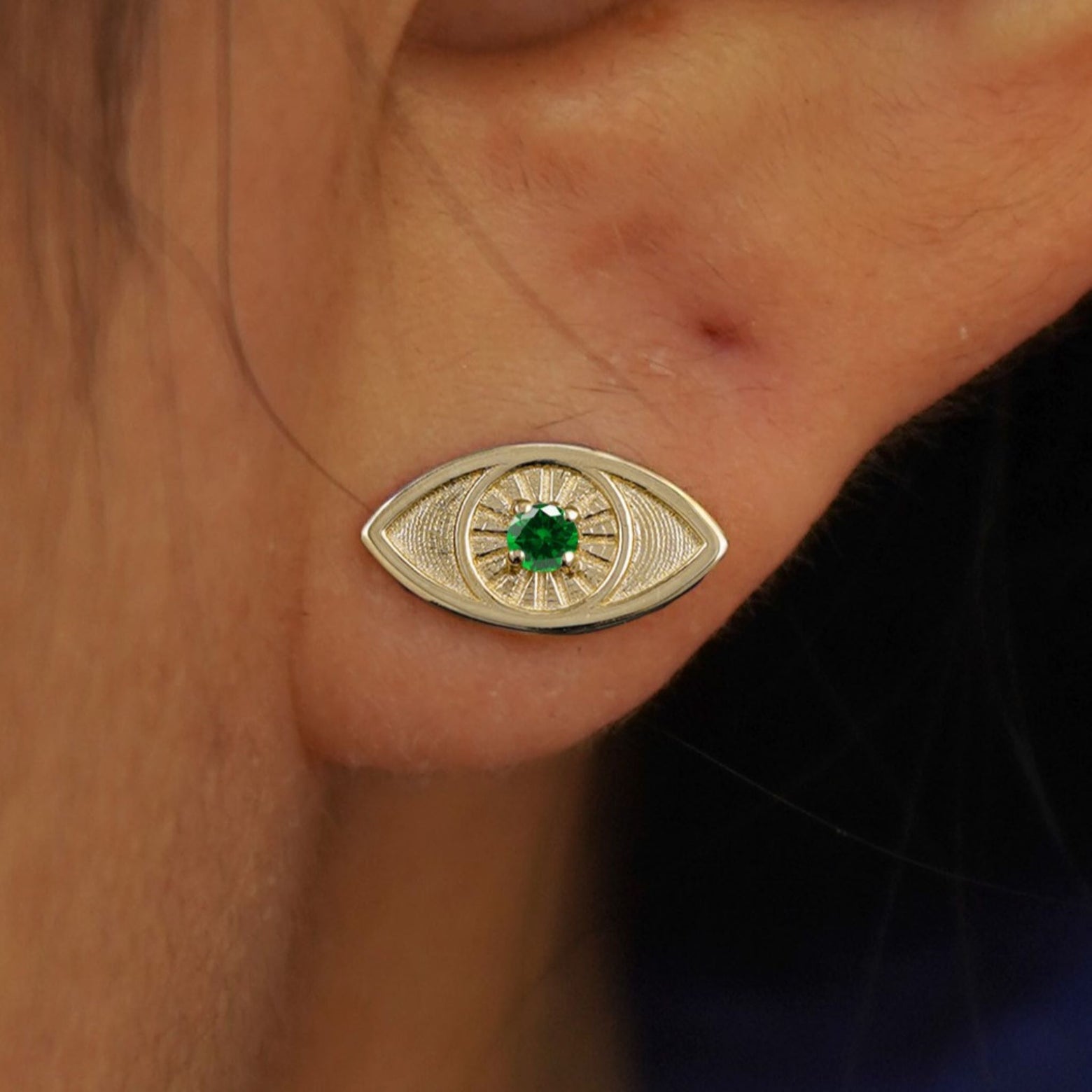 Close up view of a model's ear wearing a yellow gold emerald Evil Eye Earring