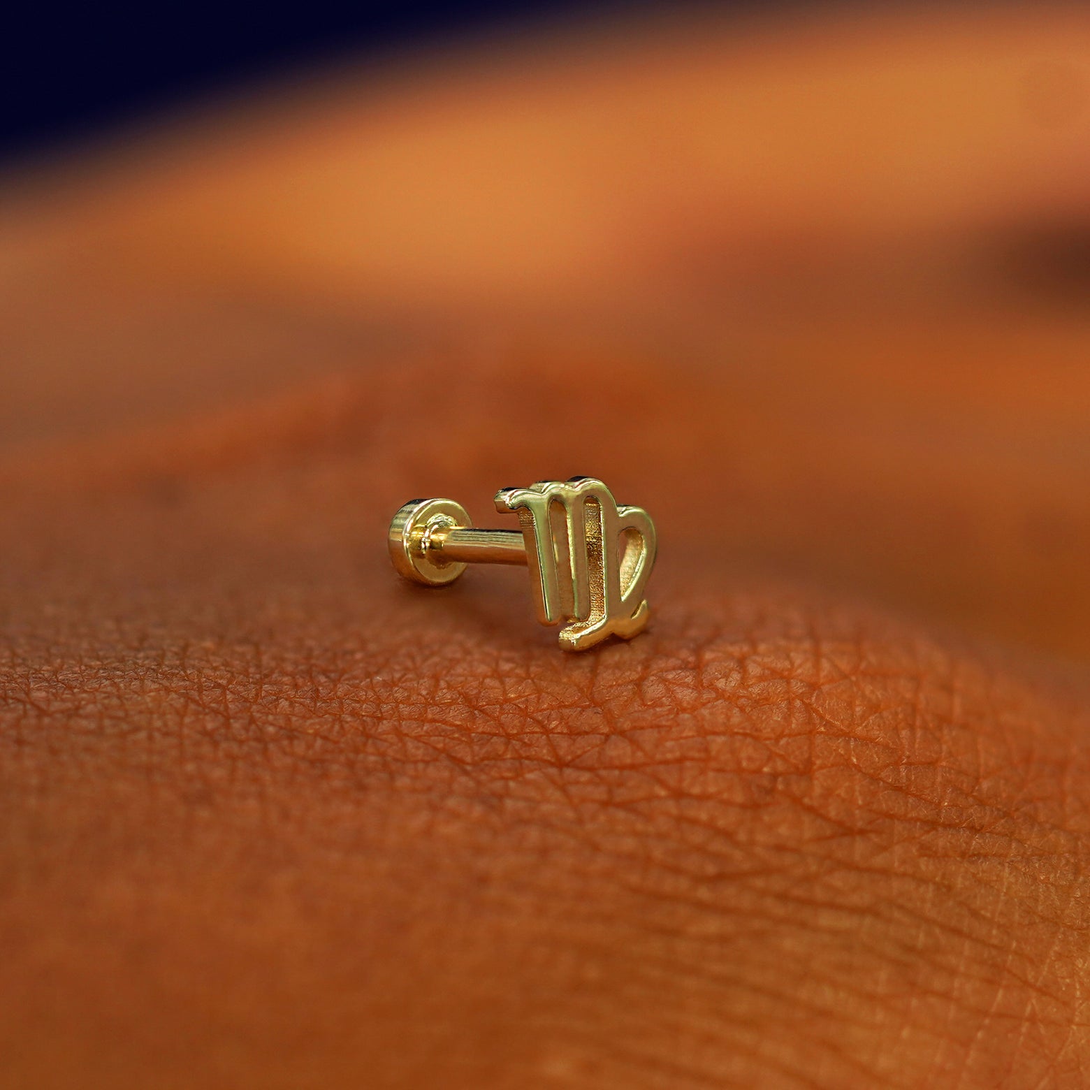 A solid 14k yellow gold Virgo Horoscope Flatback Piercing resting on the back of a model's hand