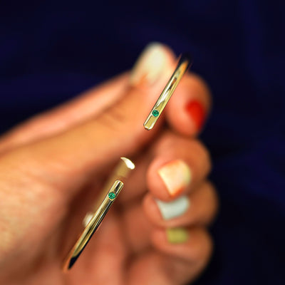 A model holding a 14k yellow gold emerald Open Bangle Bracelet to show the gap in the bangle