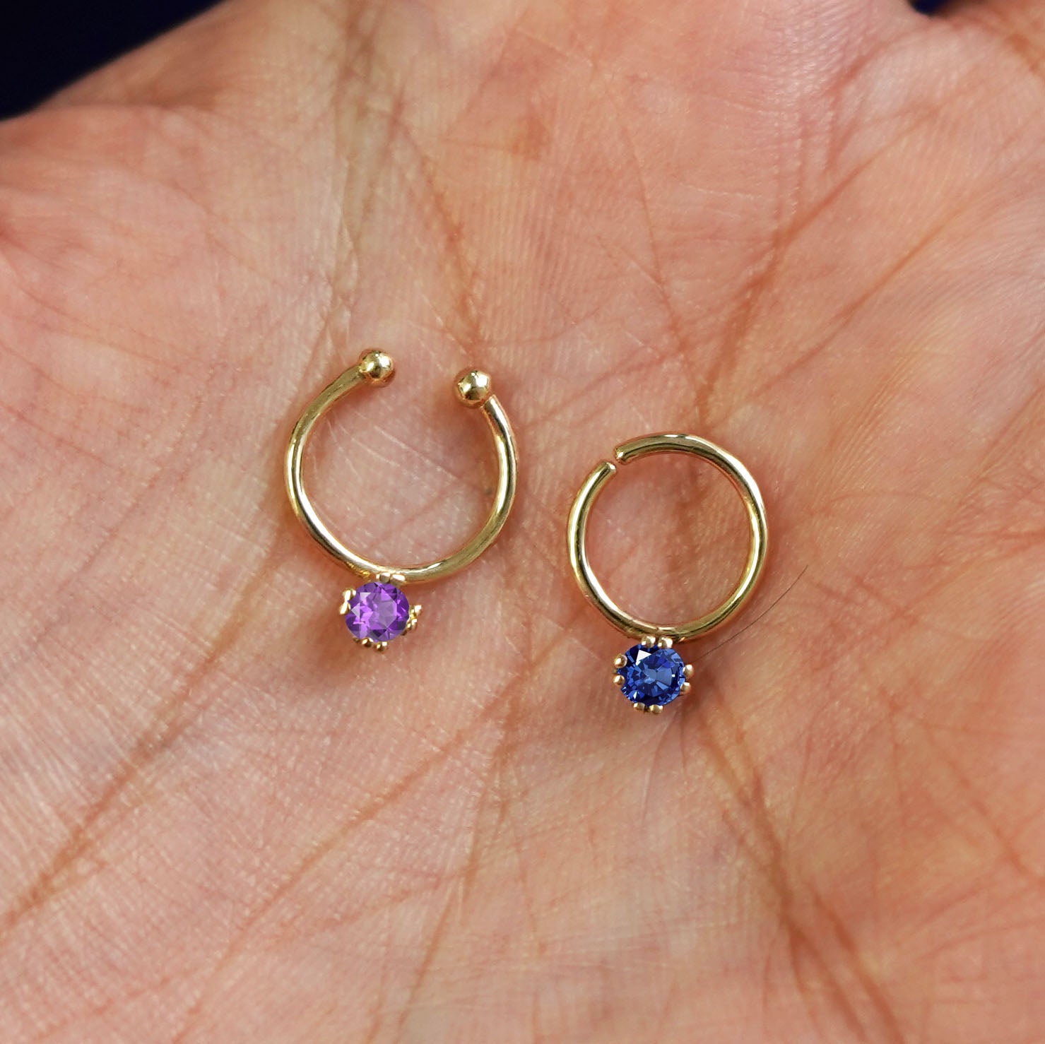 One Non-Pierced amethyst and one Pierced sapphire Gemstone Septum both in 8mm resting in the palm of a model's hand