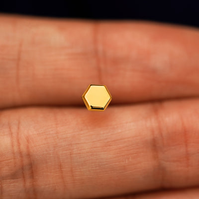 A solid 14k yellow gold Hexagon Earring in between a model's fingers