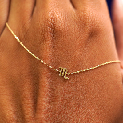 A solid gold Scorpio Horoscope Bracelet resting on the back of a model's hand