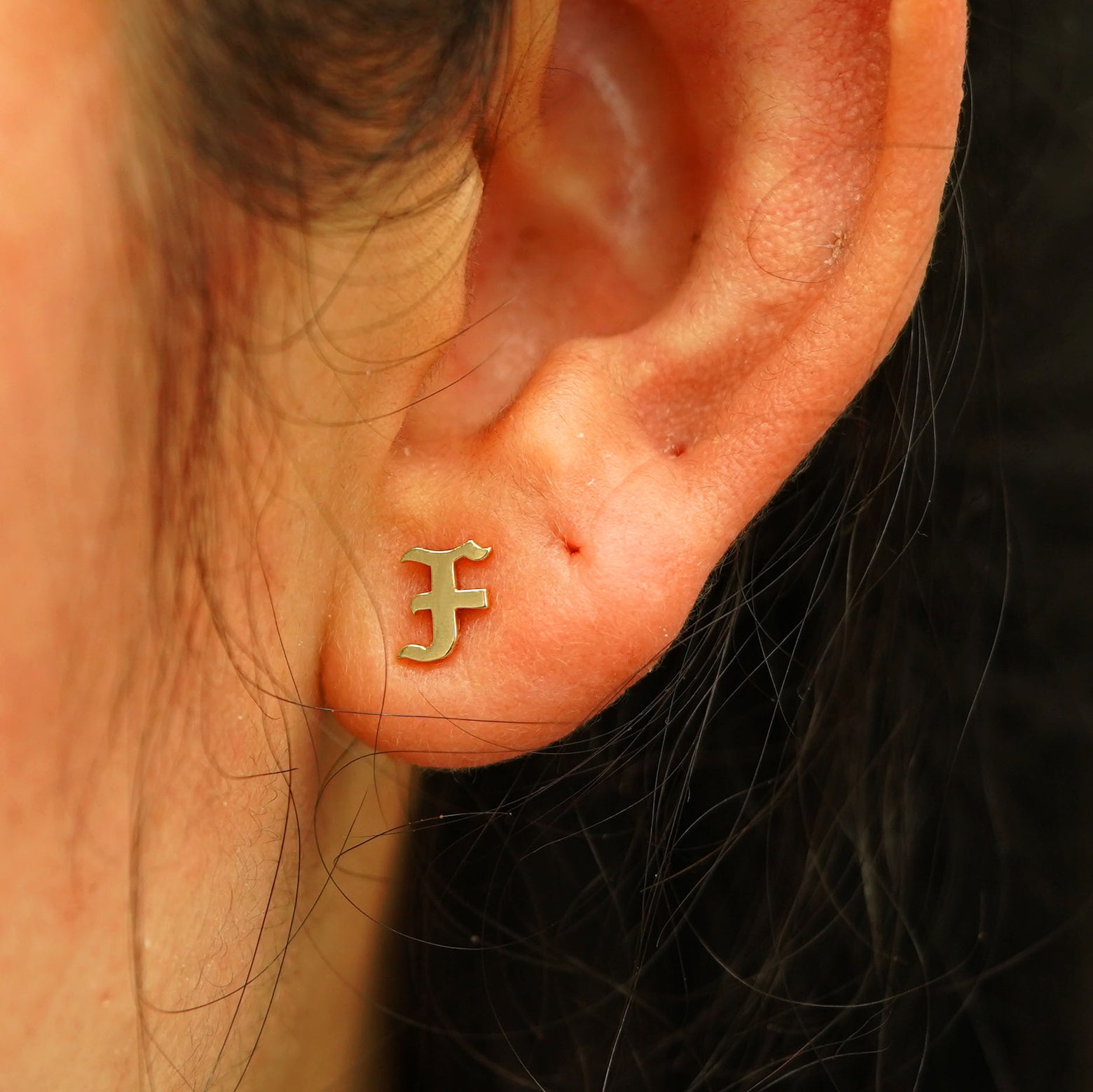 A model's ear wearing a 14k yellow gold Initial Earring in the letter F