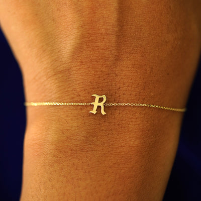 Close up view of a model's wrist wearing a 14k solid yellow gold Initial Bracelet in the letter R