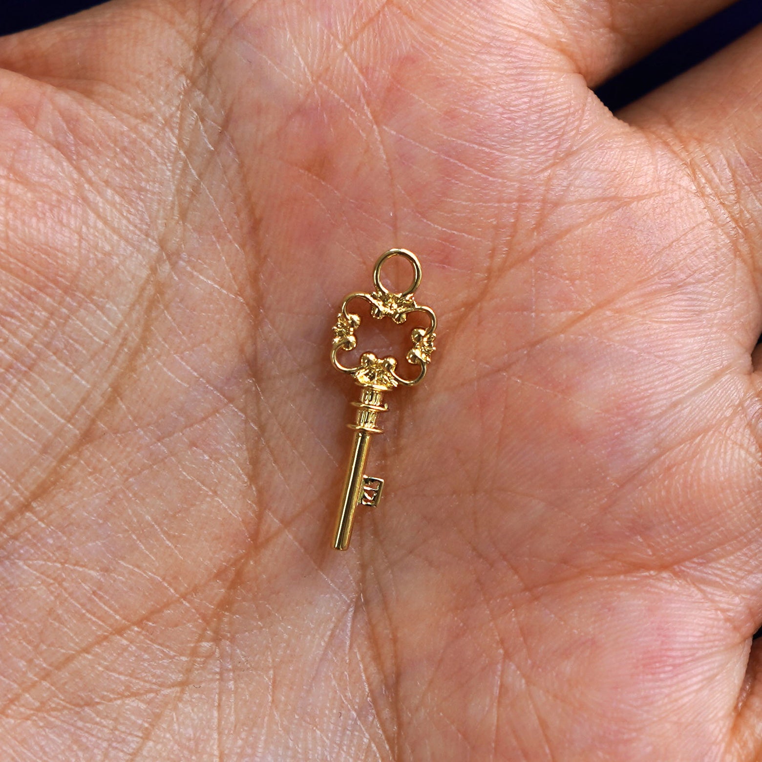 A solid gold Key Charm for earring resting in a model's palm