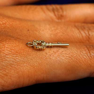 A 14k yellow gold Key Charm for earring balancing on the back of a model's finger