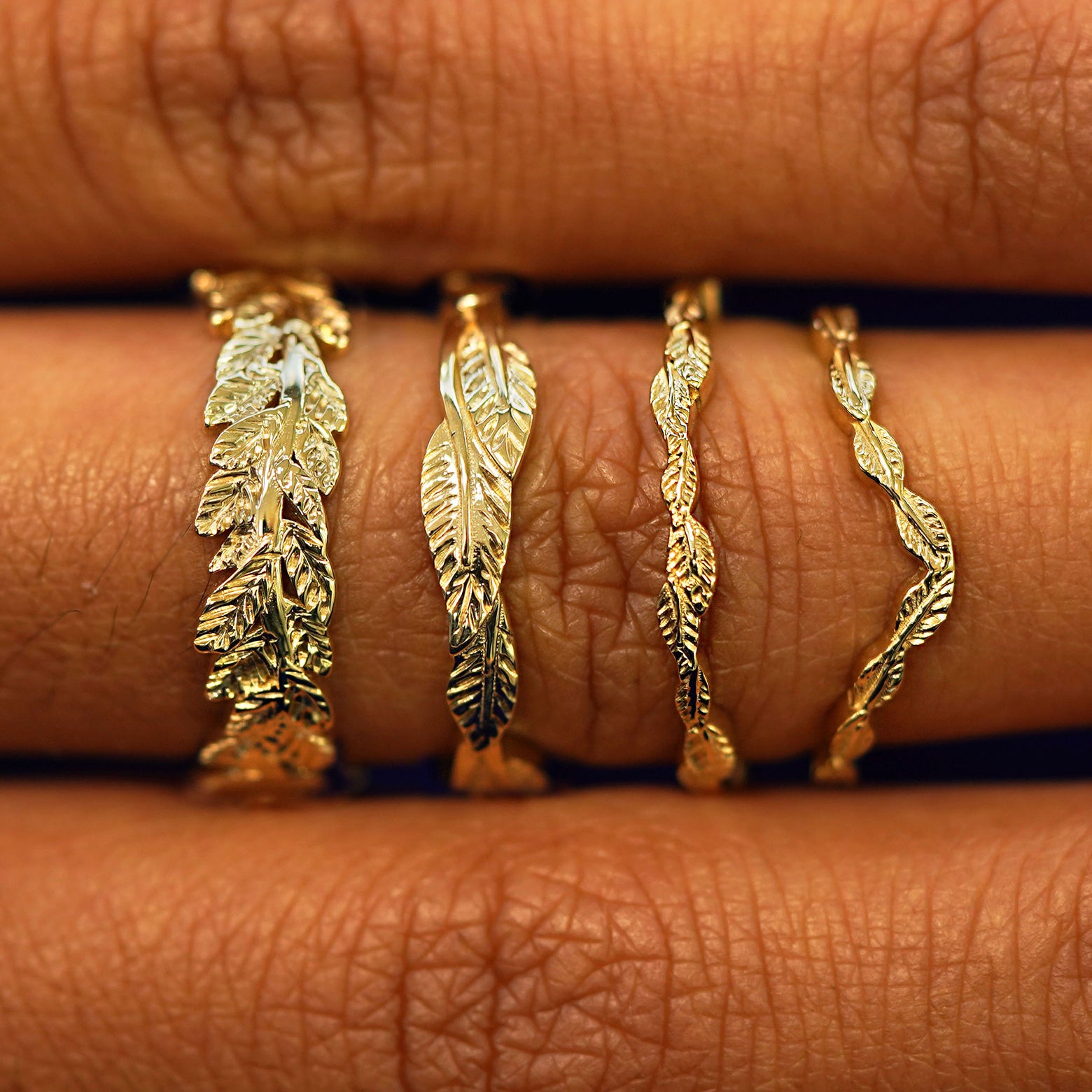 A finger wearing a yellow gold  Chevron Leaves Band, Thin Leaves Band, Thick Leaves Band, and Double Leaves Band stacked 