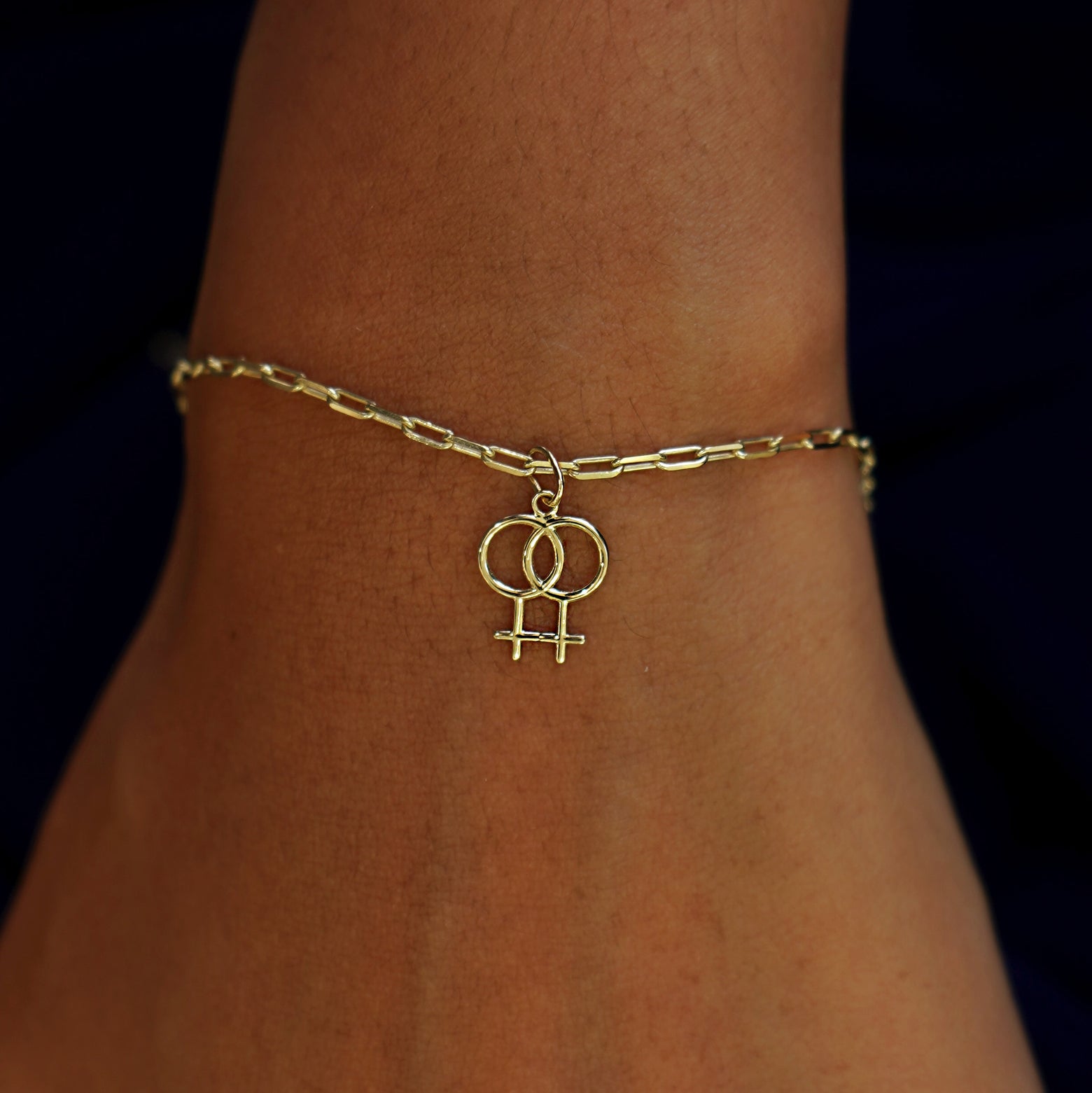 A model's wrist wearing a yellow gold Lesbian Symbol Charm on a Butch Bracelet