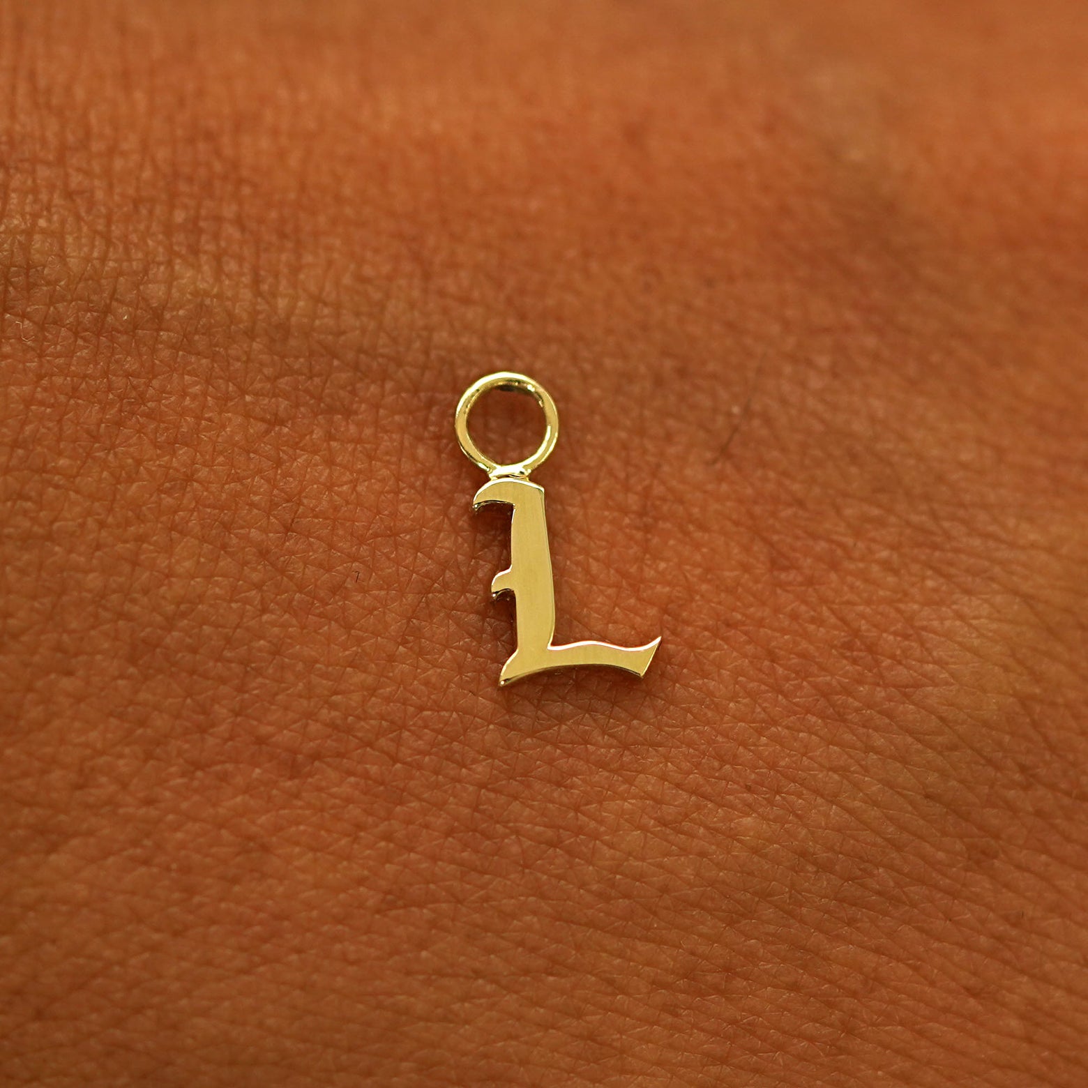A solid 14k gold Initial Charm for earring in the letter L laying on the back of a model's hand
