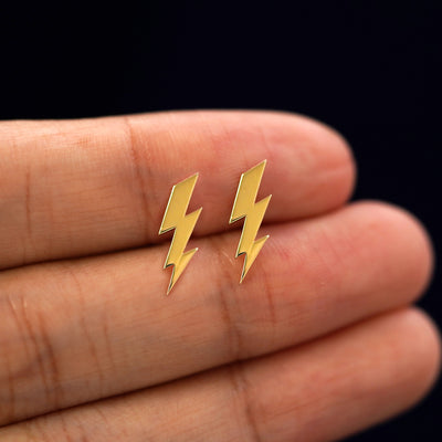 A model's hand holding a pair of recycled 14k gold Lightning Bolt Earrings